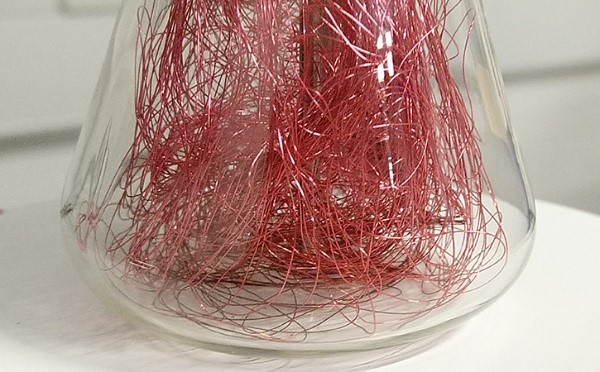 A photo of 61 metres of a red very thin copper wire with a diameter of 140 microns that is randomly tucked inside a conical glass flask to ensure that it is uniformly heated.